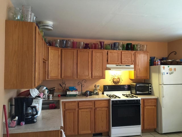 6121 12th Ave, Kenosha, WI 53143 - kitchen with gas range oven, freestanding refrigerator, under cabinet range hood, light countertops, and brown cabinetry