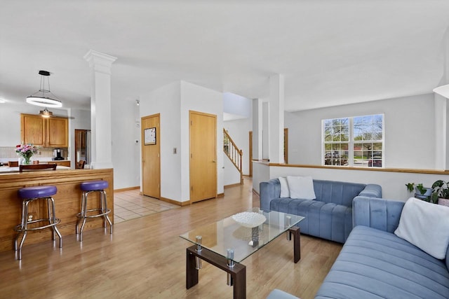 living room featuring light wood finished floors, stairs, baseboards, and decorative columns