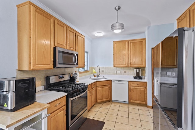kitchen with appliances with stainless steel finishes, a sink, light countertops, tasteful backsplash, and light tile patterned floors