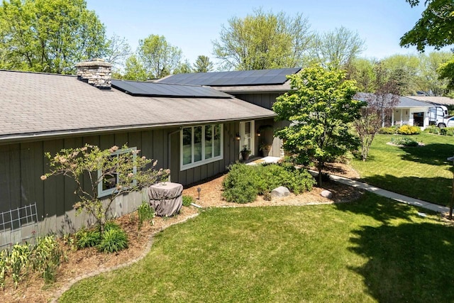 5402 Comanche Way, Madison, WI 53704 - view of front facade featuring board and batten siding, a front lawn, roof mounted solar panels, a chimney, and a shingled roof