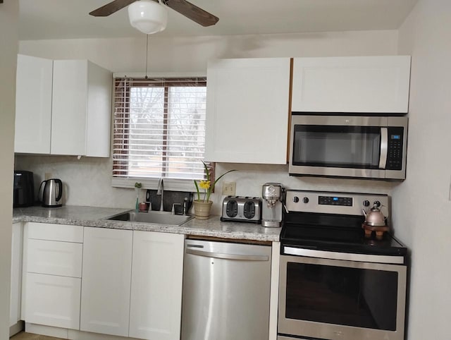 kitchen featuring stainless steel appliances, a sink, white cabinets, and ceiling fan