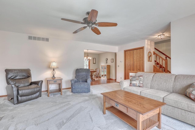 living room with stairs, light colored carpet, a chandelier, ceiling fan, and baseboards