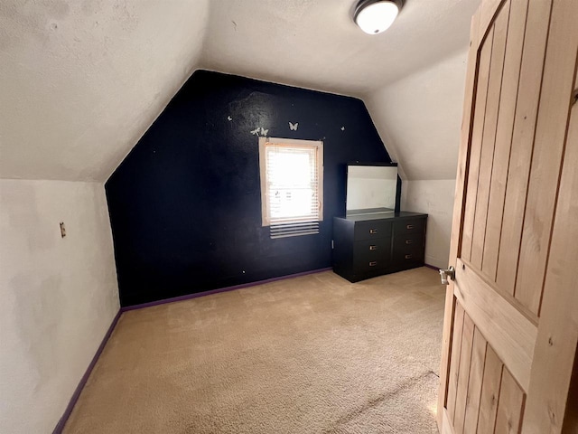 additional living space featuring light carpet, vaulted ceiling, baseboards, and a textured ceiling