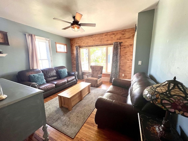 living room with a ceiling fan, light wood-style flooring, plenty of natural light, and wood walls