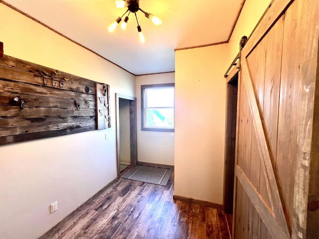 corridor with a barn door, a chandelier, wood finished floors, baseboards, and crown molding