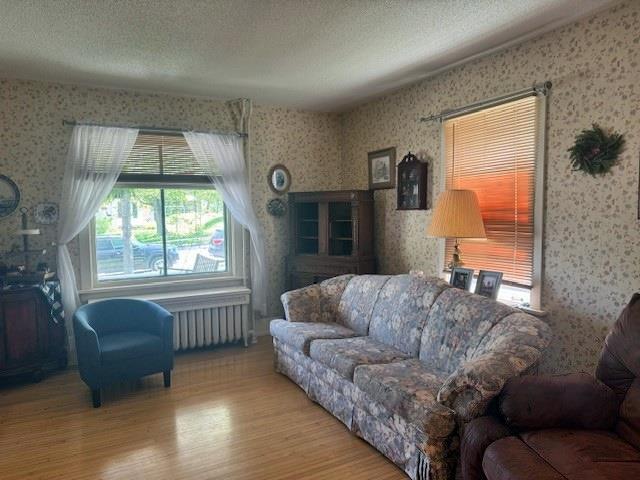 110 Hewett St, Neillsville, WI 54456 - living area with wallpapered walls, wood finished floors, radiator, and a textured ceiling
