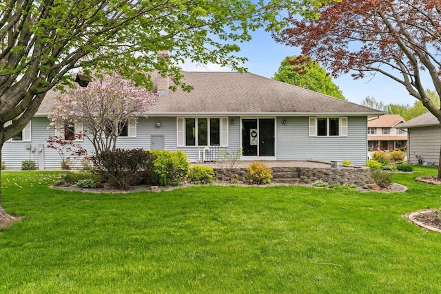 rear view of house featuring a lawn, a chimney, and a shingled roof