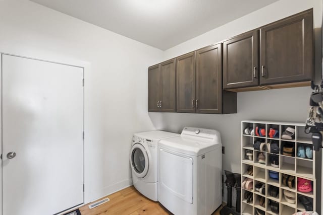 clothes washing area with separate washer and dryer, cabinet space, light wood finished floors, and baseboards