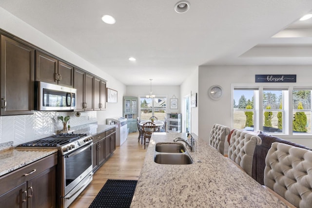 kitchen featuring stainless steel appliances, a sink, open floor plan, dark brown cabinetry, and recessed lighting