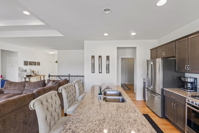 kitchen featuring a sink, open floor plan, dark brown cabinets, stainless steel appliances, and light stone countertops