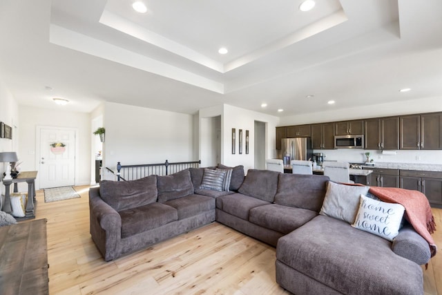 living room with a raised ceiling, light wood-type flooring, and recessed lighting