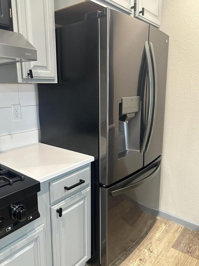 1341 S Wilson Ave Unit 10-4, Hartford, WI 53027 - kitchen featuring stainless steel fridge with ice dispenser, light wood-style floors, wall chimney exhaust hood, light countertops, and white cabinetry