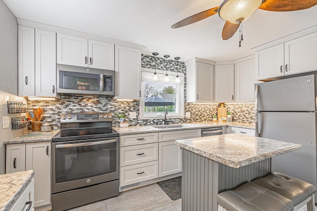 kitchen with appliances with stainless steel finishes, a sink, decorative backsplash, white cabinets, and a kitchen island