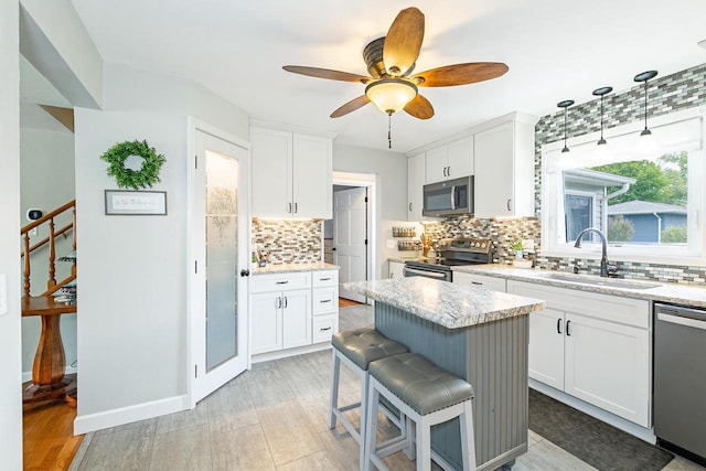 kitchen with appliances with stainless steel finishes, a sink, tasteful backsplash, white cabinetry, and a breakfast bar area