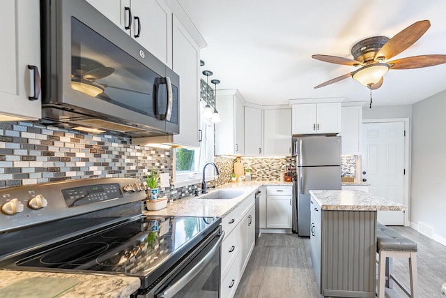 kitchen featuring appliances with stainless steel finishes, a sink, light wood finished floors, and a center island
