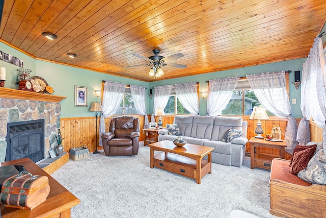 carpeted living area featuring a wainscoted wall, plenty of natural light, a ceiling fan, wood ceiling, and a fireplace