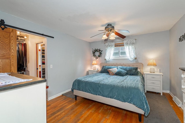 bedroom featuring a barn door, wood finished floors, baseboards, and a walk in closet