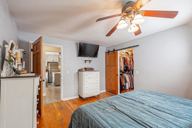 bedroom with freestanding refrigerator, light wood-style floors, a barn door, a ceiling fan, and a closet