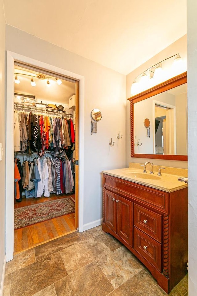 bathroom with vanity, baseboards, a spacious closet, and stone finish flooring