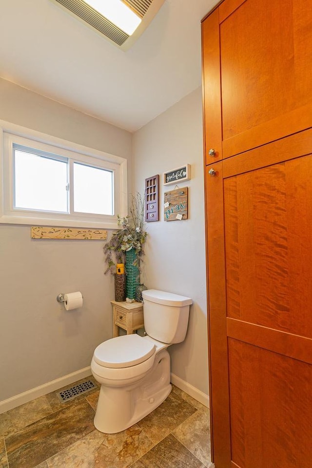 bathroom with toilet, baseboards, and stone finish flooring