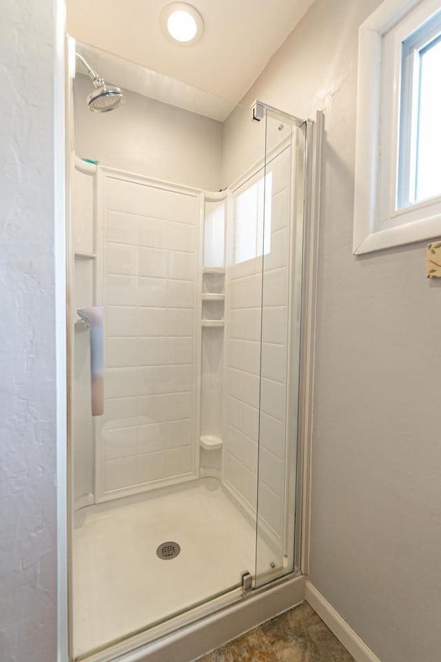 full bathroom with healthy amount of natural light, a shower stall, and baseboards