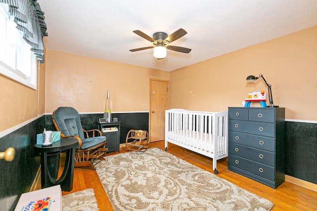 bedroom featuring wood finished floors, a crib, and ceiling fan