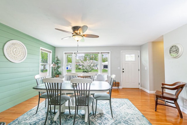 dining area with a ceiling fan, wood walls, light wood-style flooring, and baseboards