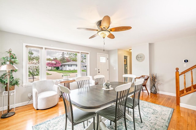dining room featuring a ceiling fan, baseboards, light wood-type flooring, and stairs