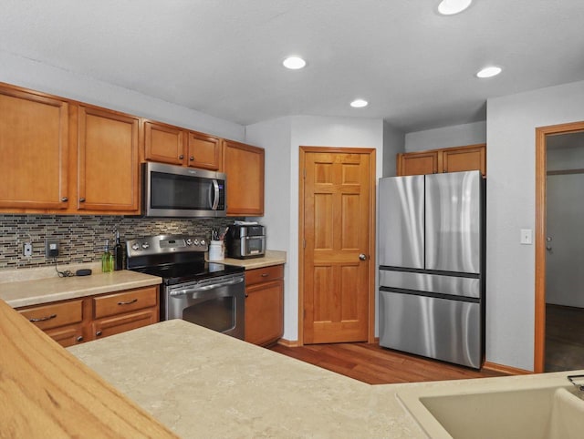1537 Whitewater Dr, West Bend, WI 53095 - kitchen featuring appliances with stainless steel finishes, brown cabinetry, light countertops, decorative backsplash, and wood finished floors