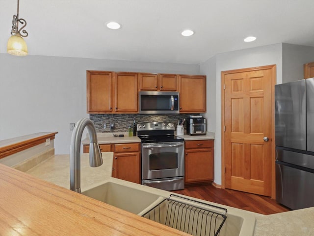1537 Whitewater Dr, West Bend, WI 53095 - kitchen with appliances with stainless steel finishes, light countertops, dark wood-type flooring, decorative backsplash, and decorative light fixtures