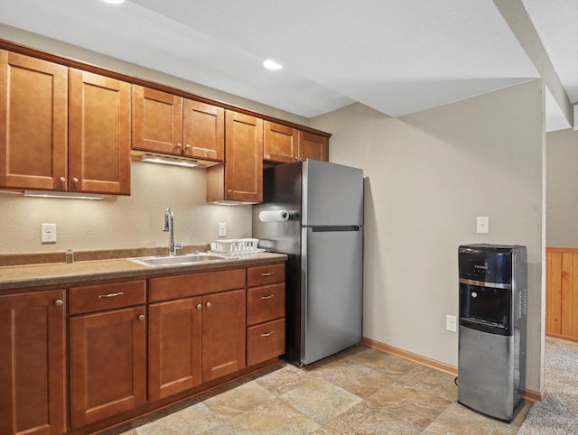 1537 Whitewater Dr, West Bend, WI 53095 - kitchen with freestanding refrigerator, a sink, brown cabinets, baseboards, and light stone finish floors