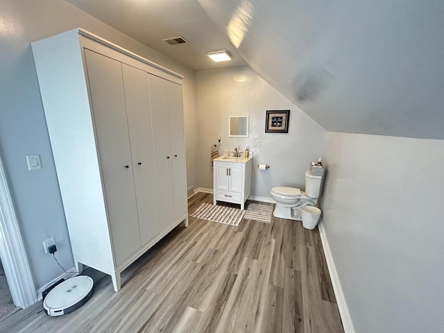 bathroom with wood finished floors, lofted ceiling, toilet, vanity, and baseboards