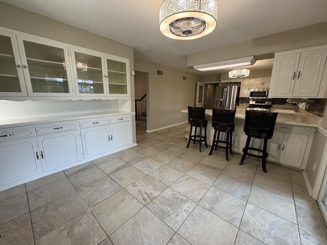 kitchen featuring stainless steel appliances, glass insert cabinets, white cabinetry, a peninsula, and a kitchen breakfast bar