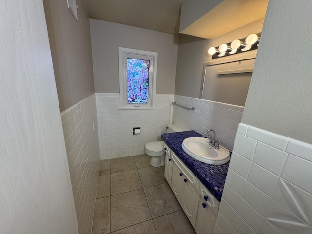 bathroom with tile walls, tile patterned flooring, vanity, toilet, and a wainscoted wall
