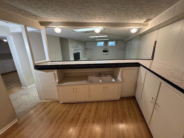 kitchen with a sink, light wood-type flooring, light countertops, baseboards, and white cabinets