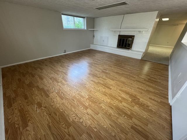unfurnished living room with wood finished floors, a fireplace, baseboards, and a textured ceiling