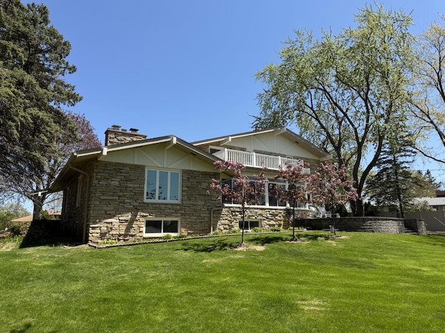 rear view of property with a balcony, a chimney, stone siding, and a lawn