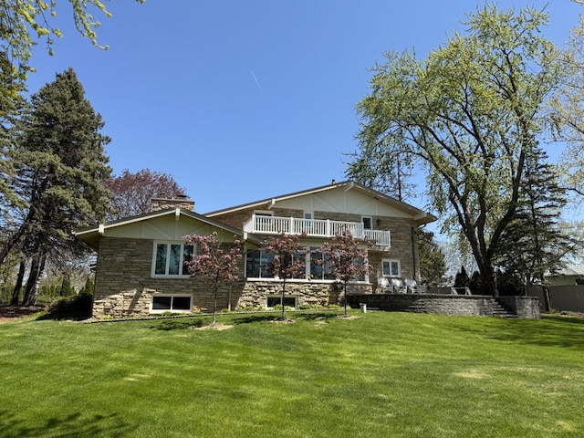 rear view of house with a yard, stone siding, and a balcony