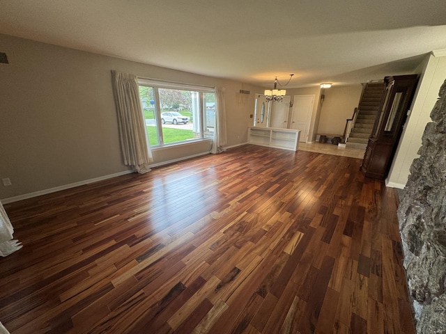 unfurnished living room with a chandelier, dark wood-style flooring, stairway, and baseboards