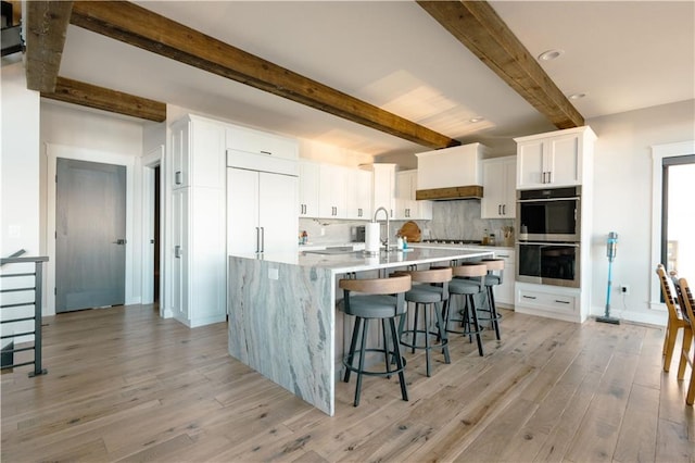 2936 W Sunset Bay, Birchwood, WI 54817 - kitchen featuring stainless steel double oven, beam ceiling, tasteful backsplash, light wood finished floors, and white cabinetry