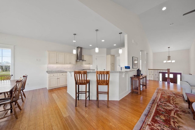 1387 Wilmington Way Unit 3-34, Lake Geneva, WI 53147 - kitchen featuring wall chimney exhaust hood, light wood-style flooring, a chandelier, a breakfast bar area, and light stone countertops