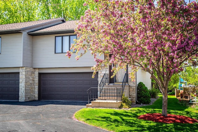 view of front of property featuring stone siding, a garage, a shingled roof, a front yard, and driveway