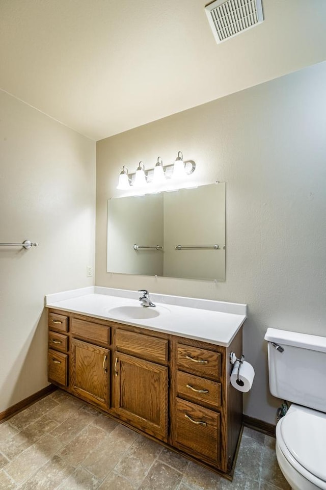 bathroom with baseboards, vanity, toilet, and stone finish flooring