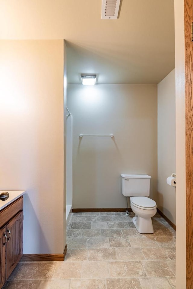 bathroom featuring baseboards, stone finish flooring, toilet, vanity, and a shower