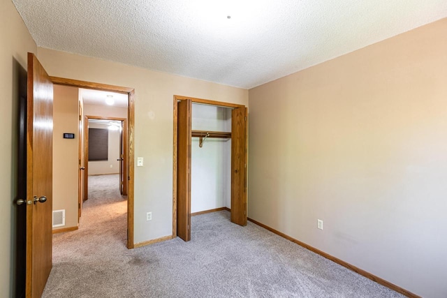 unfurnished bedroom with light carpet, a closet, a textured ceiling, and baseboards