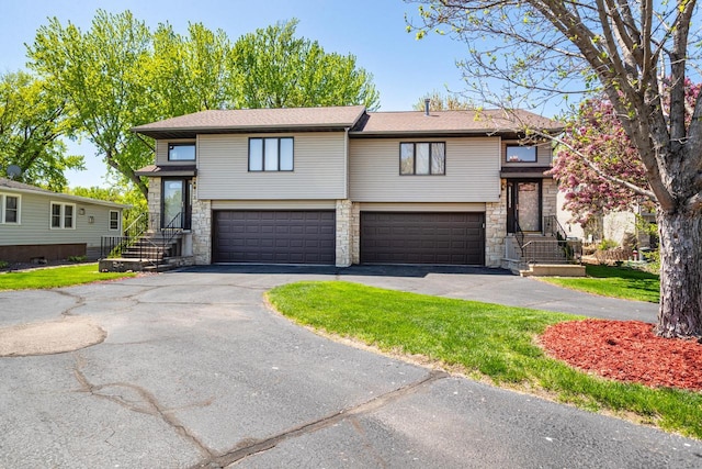 view of front of home featuring an attached garage, driveway, stone siding, and a front yard