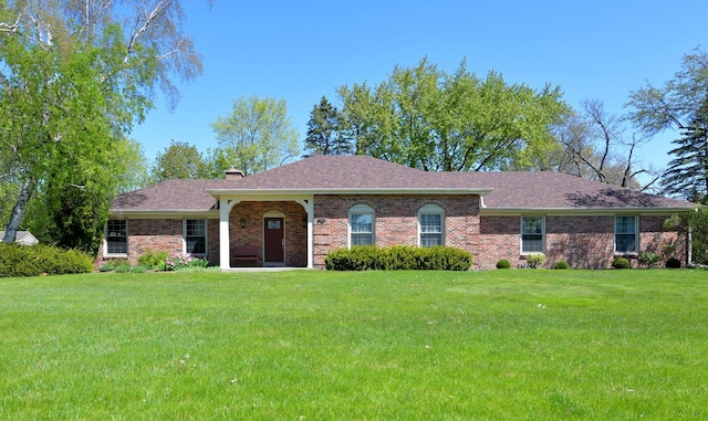 view of front of home featuring a front yard, a chimney, brick siding, and a shingled roof