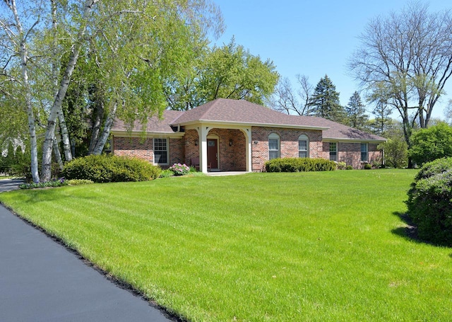 single story home featuring a front yard, brick siding, and roof with shingles