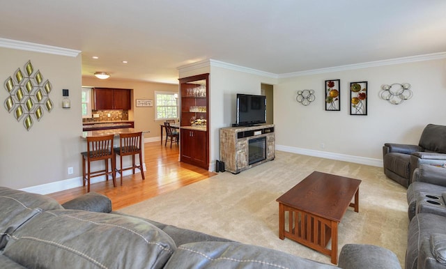 living area featuring ornamental molding, baseboards, light colored carpet, a fireplace, and light wood finished floors