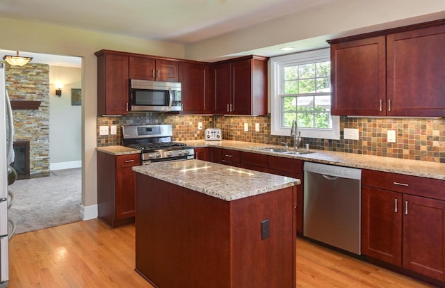 kitchen with appliances with stainless steel finishes, a sink, light stone countertops, a stone fireplace, and backsplash